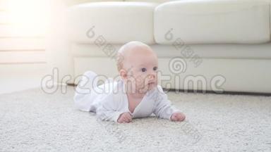 快乐的婴儿躺在地毯背景下，微笑着穿着白色衣服的婴儿女孩